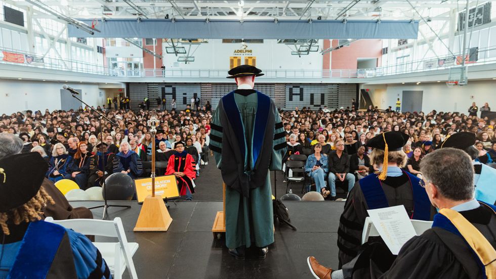 Dr. Storm addresses a large audience of students and faculty members from the stage. Behind him are other University officials.