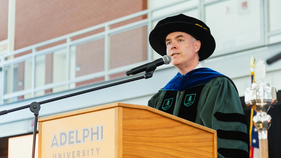 Dr. Storm, in full academic regalia, addresses students from the lectern.
