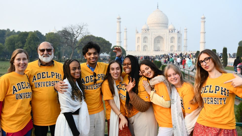 A group of students and faculty standing in front of the Taj Mahal in India wearing yellow Adelphi t-shirts