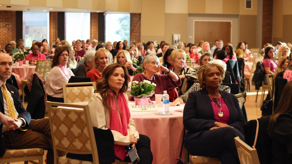 Audience seated at Celebration of Survivorship Gala event, listening attentively at round tables with flower centerpieces.
