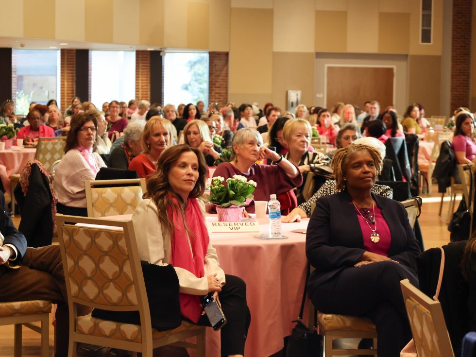 Audience seated at Celebration of Survivorship Gala event, listening attentively at round tables with flower centerpieces.