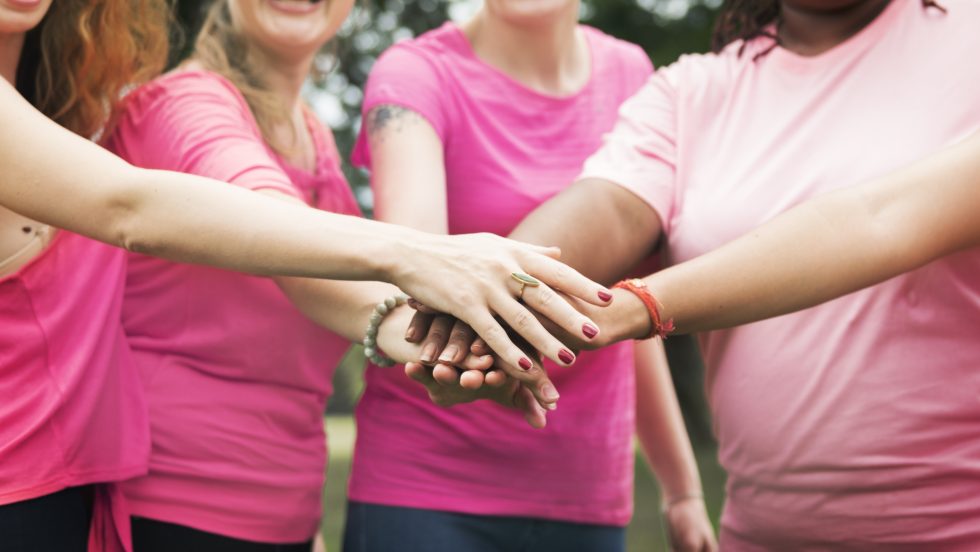 Women wearing pink and breast cancer ribbons with hands in for teamwork