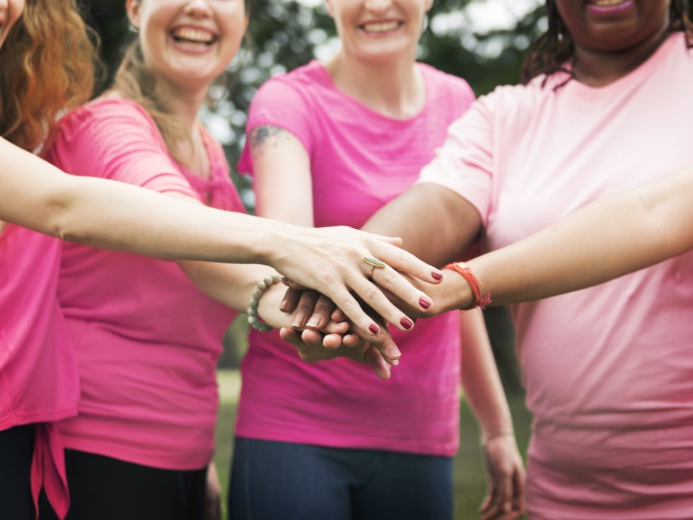Women wearing pink and breast cancer ribbons with hands in for teamwork