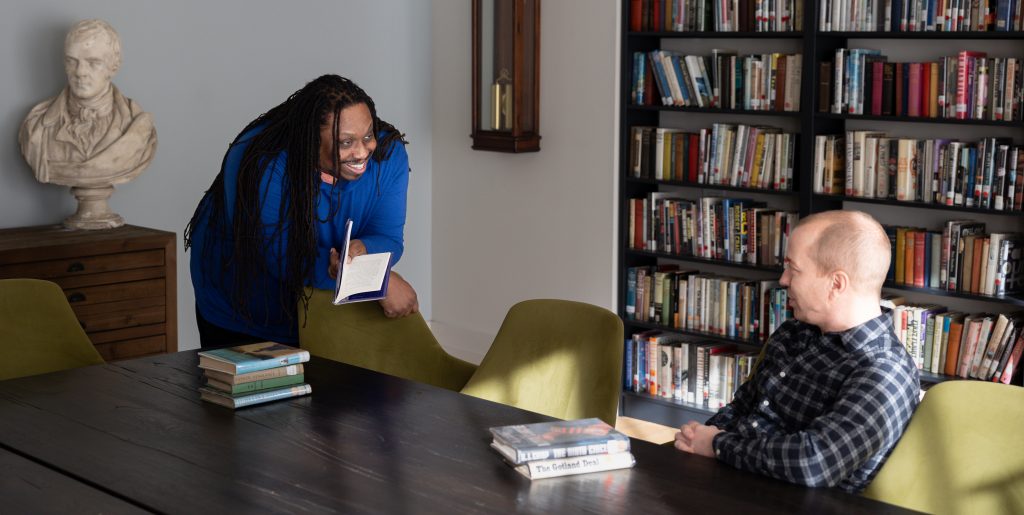 Two student in a room talking at a table.