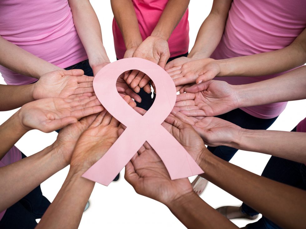 Women wearing pink and breast cancer ribbons with hands in for teamwork