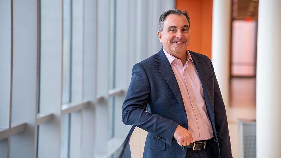 Man in a blue suit and pink shirt smiling, leaning on a railing
