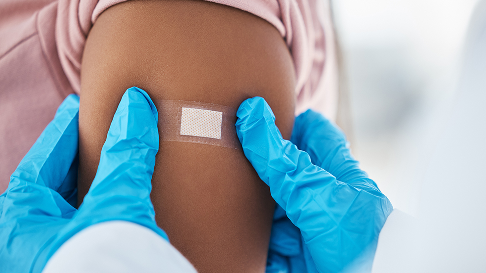 Close-up of a bandage being applied to an upper arm after an injection.