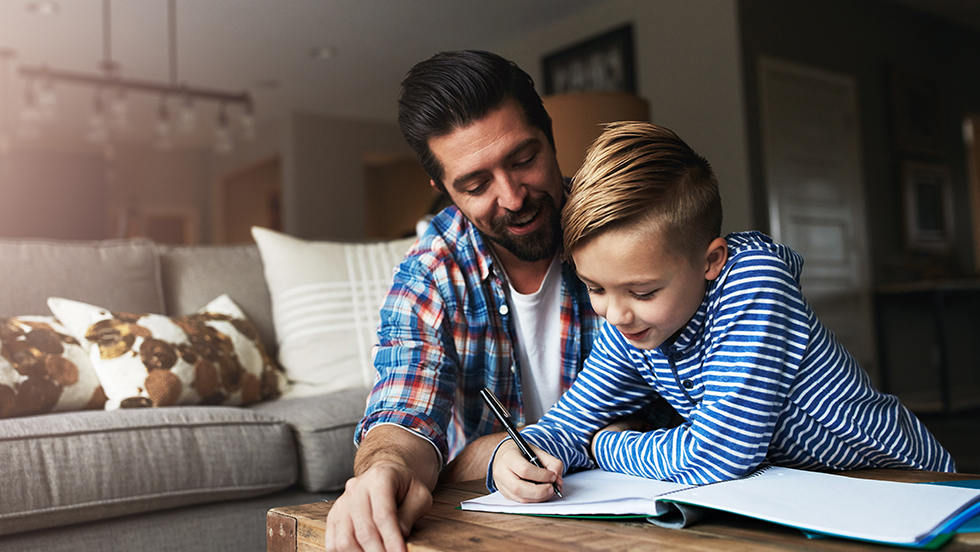 A father and his young son doing homework together in the living room.