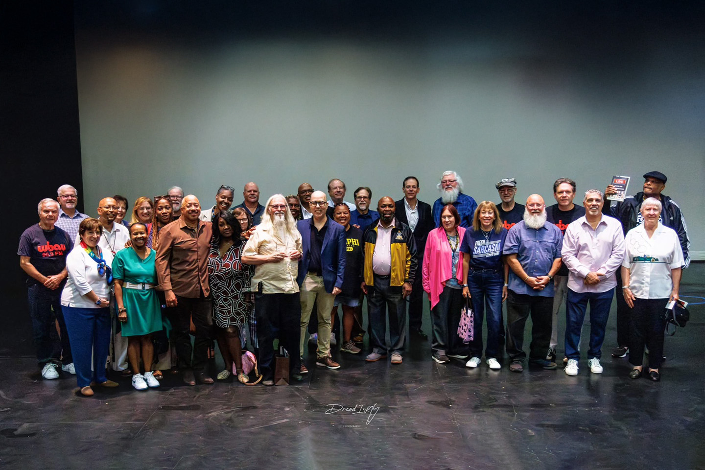 A group photo of the 32 WBAU alumni, taken on stage.