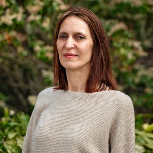 A woman with medium-length brown hair with reddish highlights wearing a beige sweater 