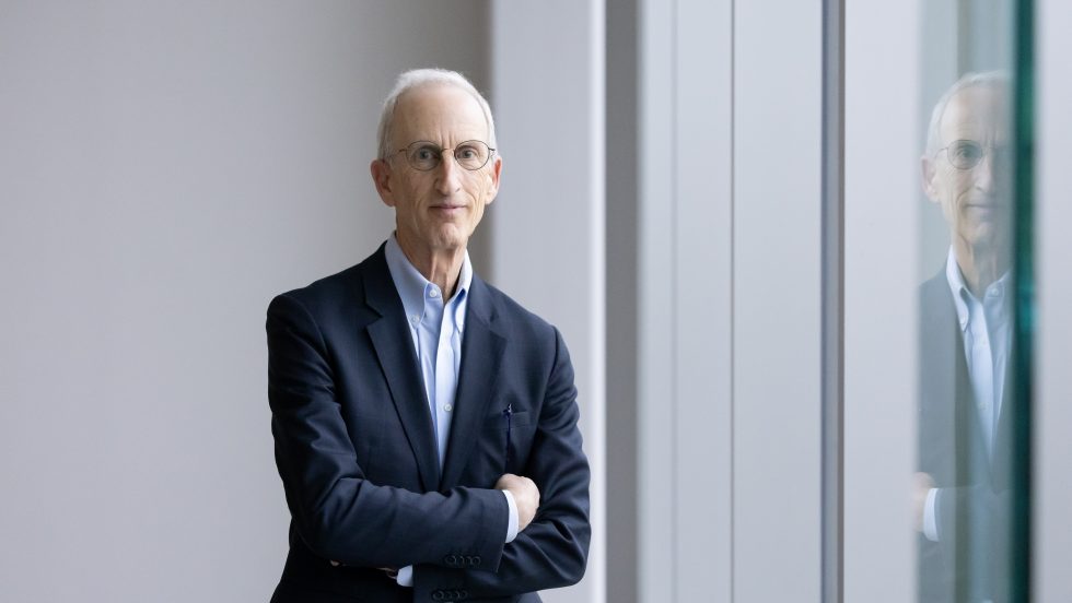 A photo of a man in a blue suit, standing with arms crossed.