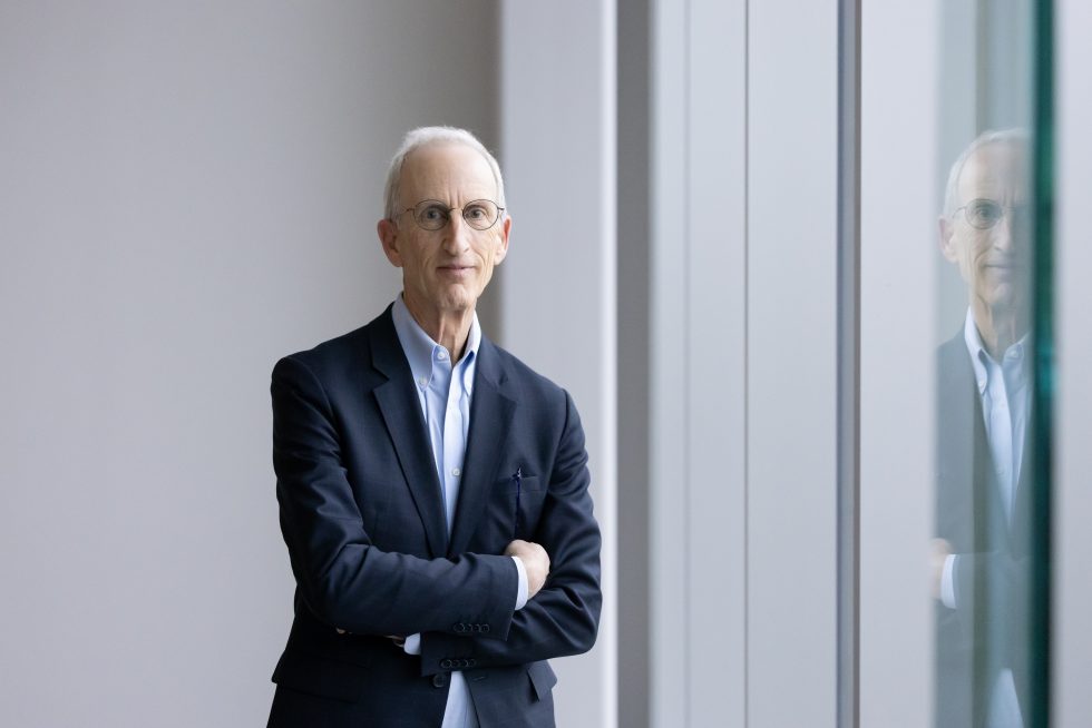 A photo of a man in a blue suit, standing with arms crossed.
