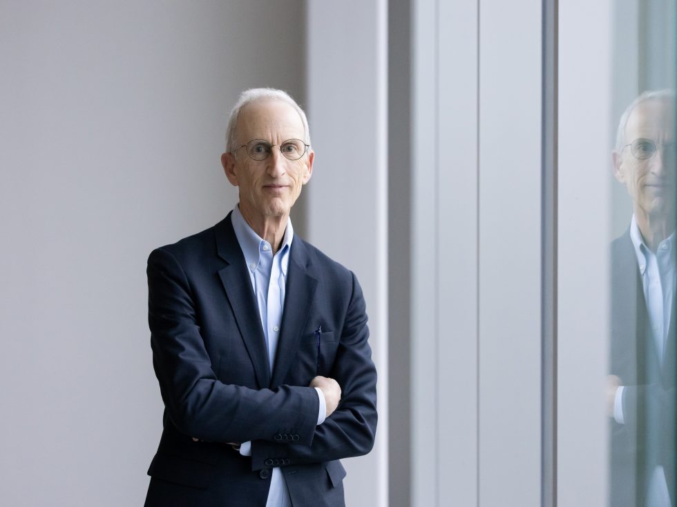 A photo of a man in a blue suit, standing with arms crossed.