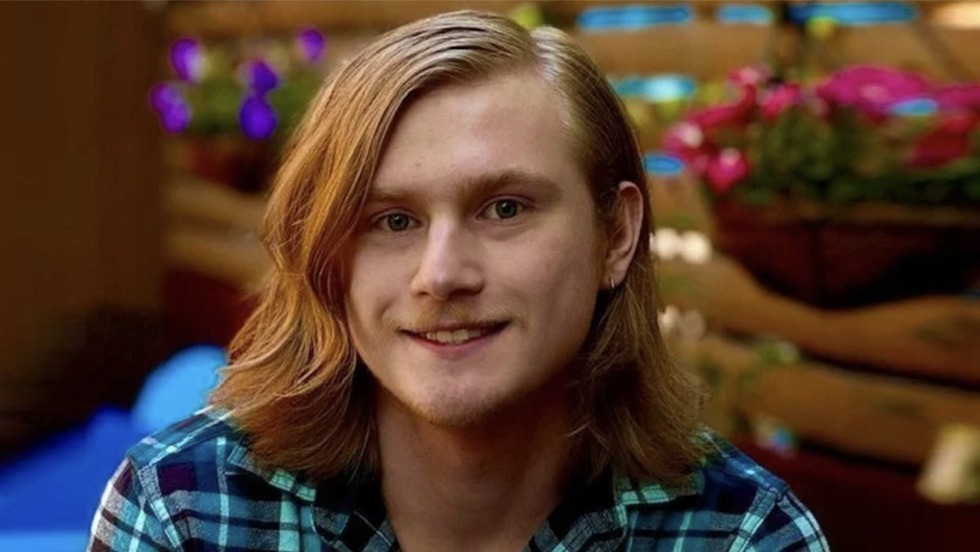 A young man with long auburn hair smiles at camera.
