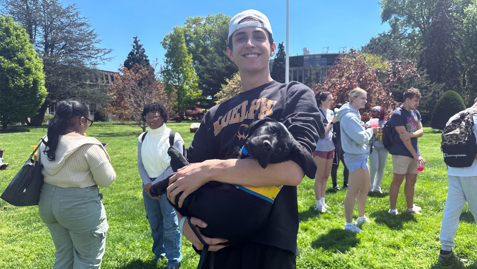 Junior James Tullo holds a black Labrador puppy in his arms, while other students gather in the background.