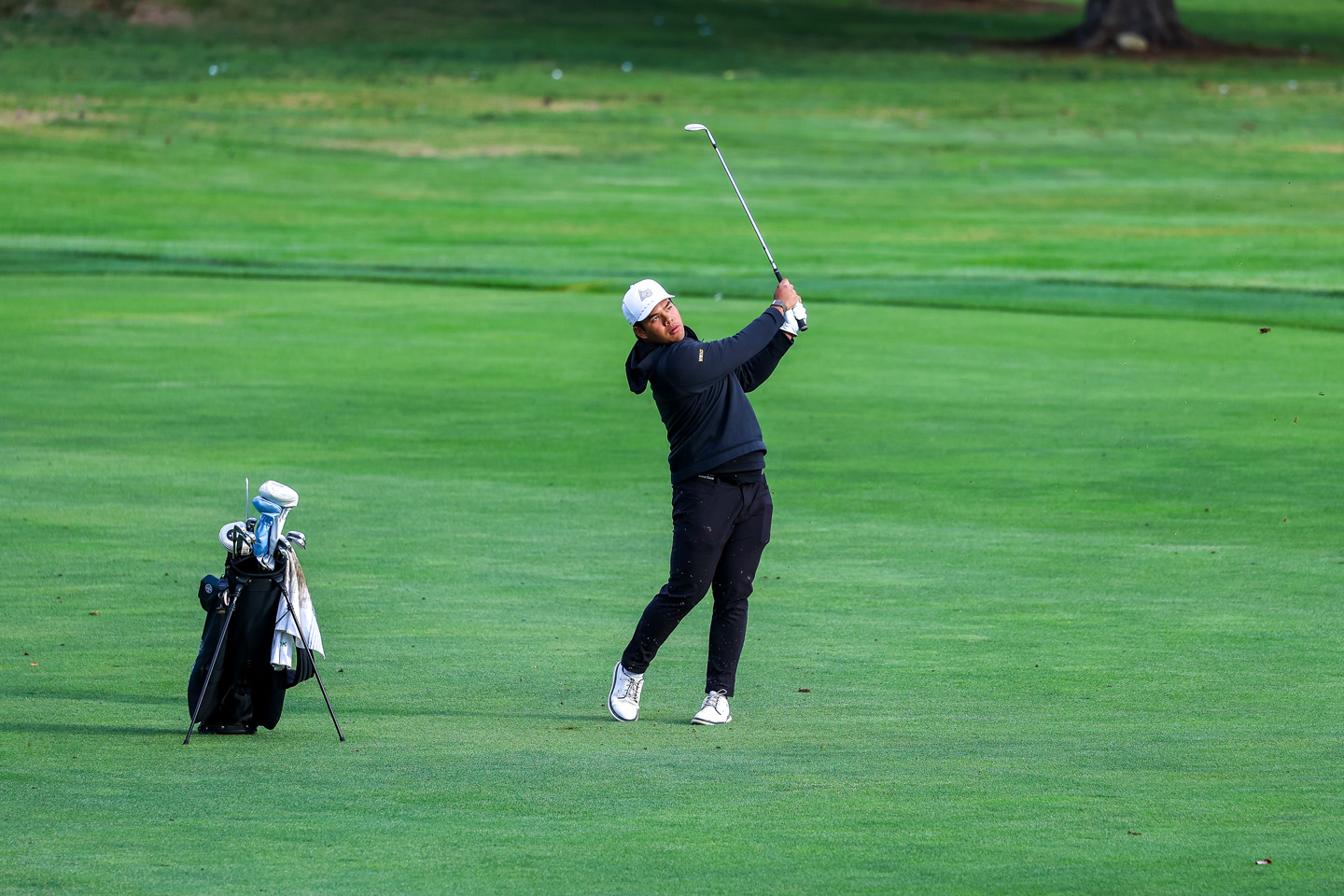 Francis Lanuza in mid swing on the greens, with his golf bag next to him.