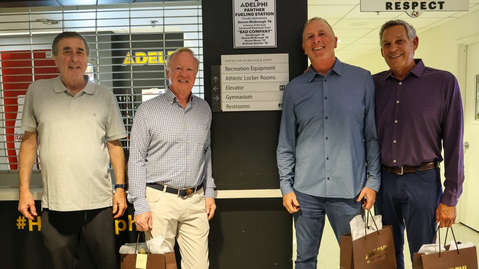 Four adult men stand smiling in front of a wall labeled “Panther Fueling Station” inside a campus recreation center.
