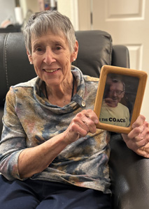 woman in gray recliner holding a framed photo of her late husband