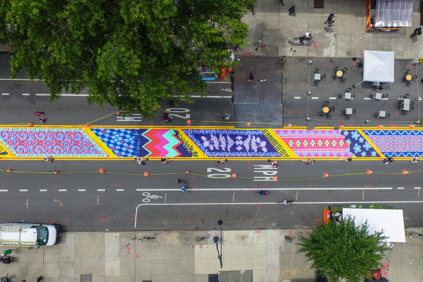 The mural, seen from above, covers a lane of traffic with colorful, painted sections based on carpet designs.