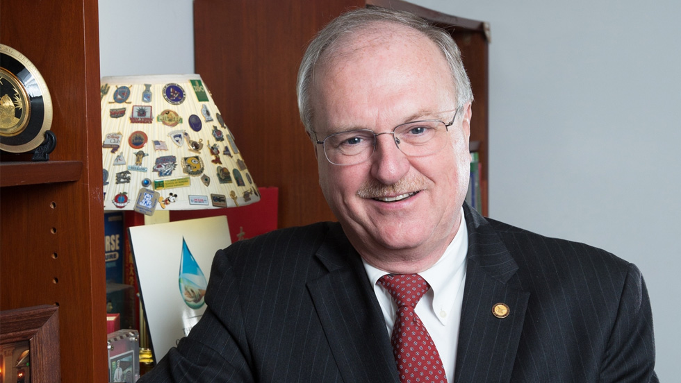 headshot of older white male in suit and red tie
