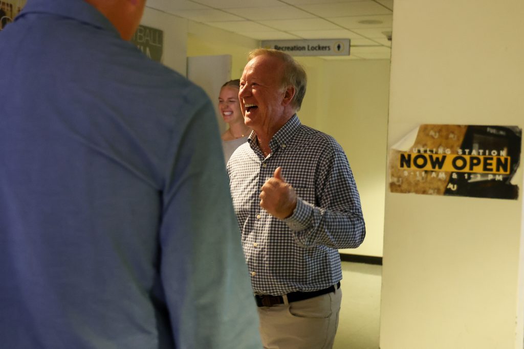 An adult man laughs while talking with others inside a campus recreation facility hallway.