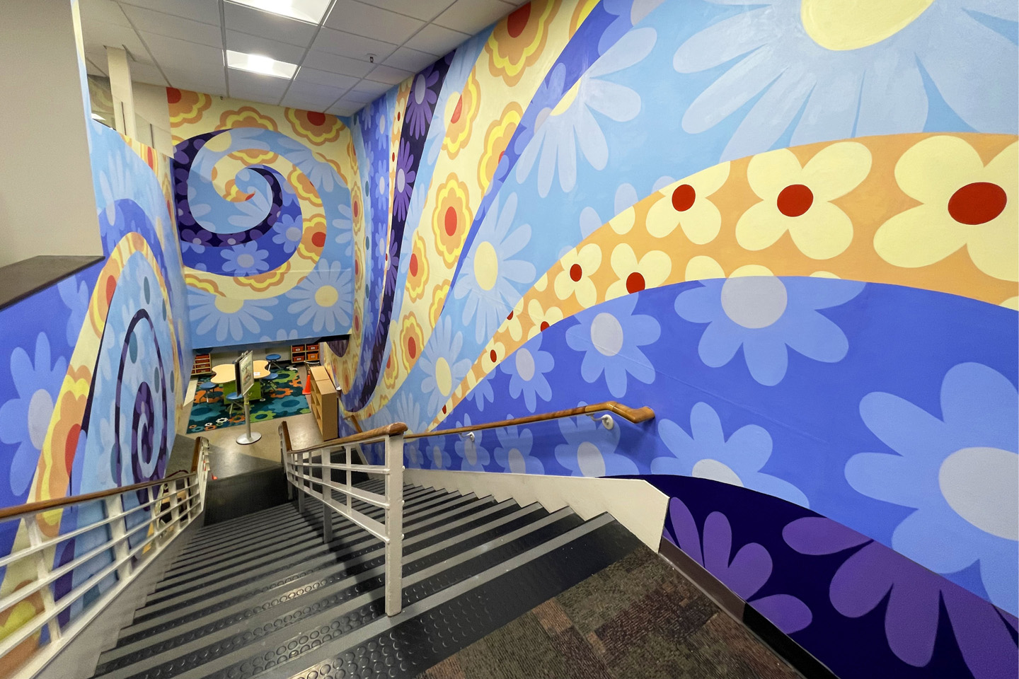 The swirling colors and floral designs of the mural coat the walls of a library staircase.