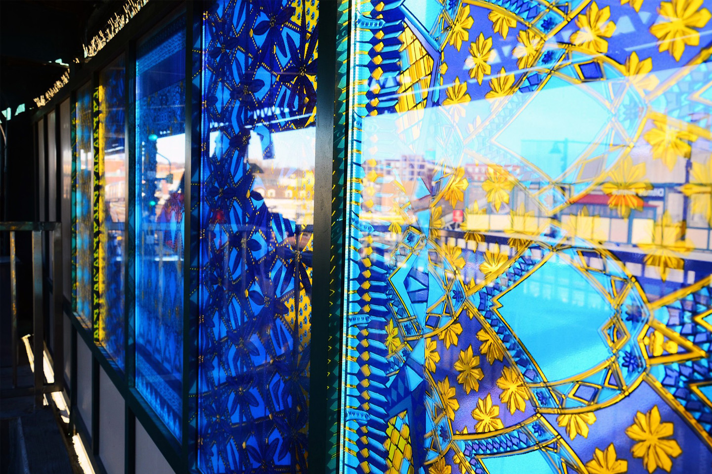 One of the compositions is seen on the subway platform, with awaiting riders next to it. The five panels are of geometric designs in blue, purple and yellow.