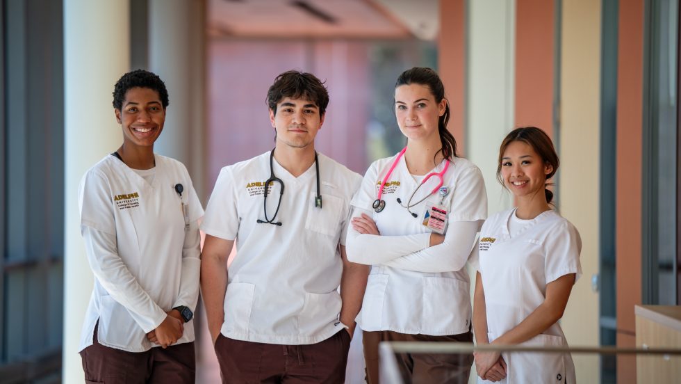Four nursing students posing together wearing white scrubs