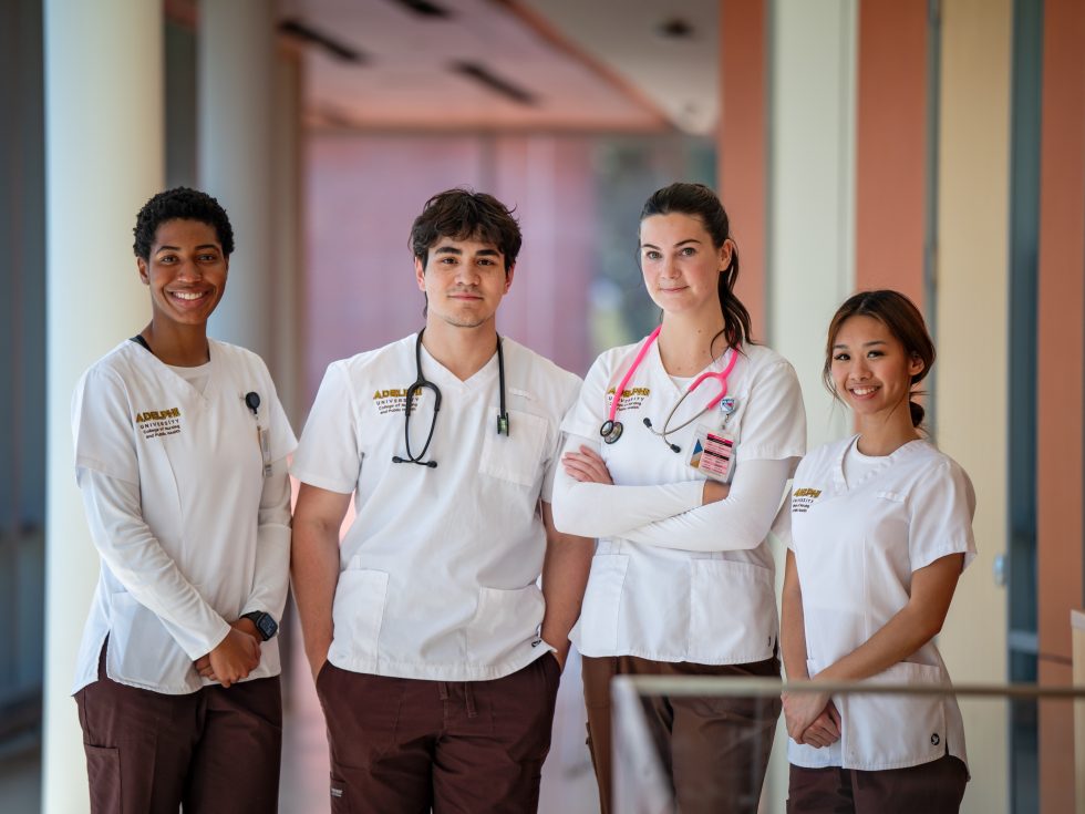 Four nursing students posing together wearing white scrubs
