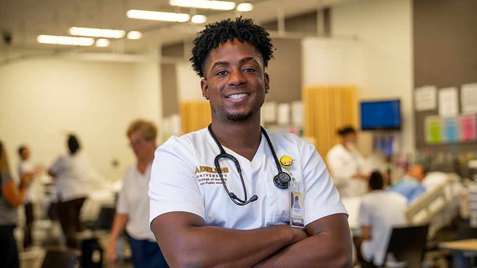 A male nursing student stands proudly in the simulation lab, arms crossed, at the College of Nursing and Public Health.
