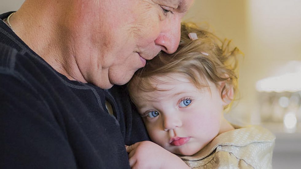 Mark W. Jordan ’63 holding and embracing his young granddaughter indoors.