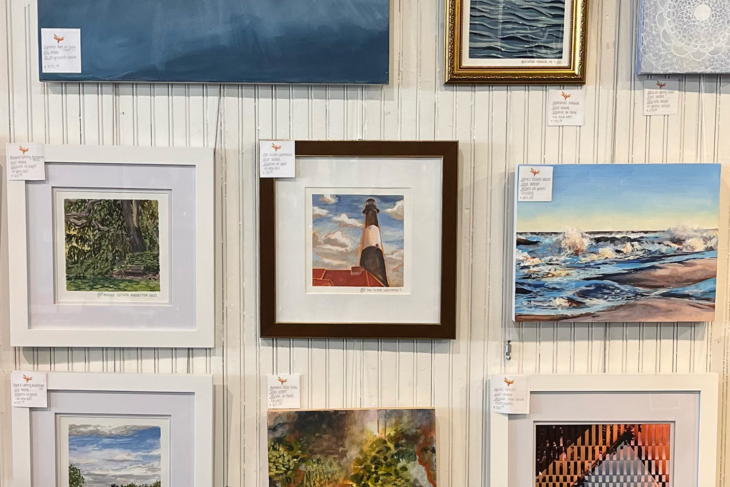 A gallery wall displaying a collection of framed and unframed artwork arranged on white vertical paneling