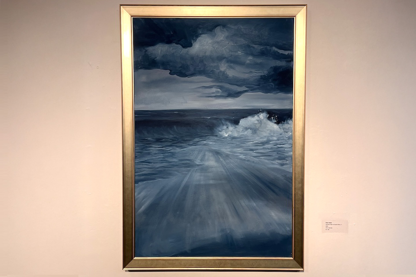 A vertically framed painting of a stormy ocean scene hangs on a gallery wall.
