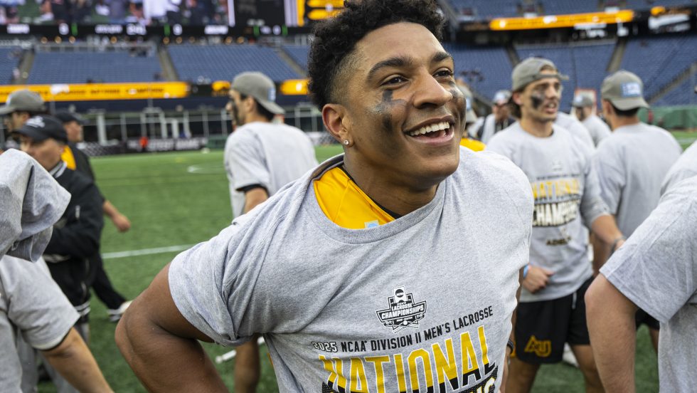 Male soccer player smiling and celebrating on the field in a sports stadium setting.