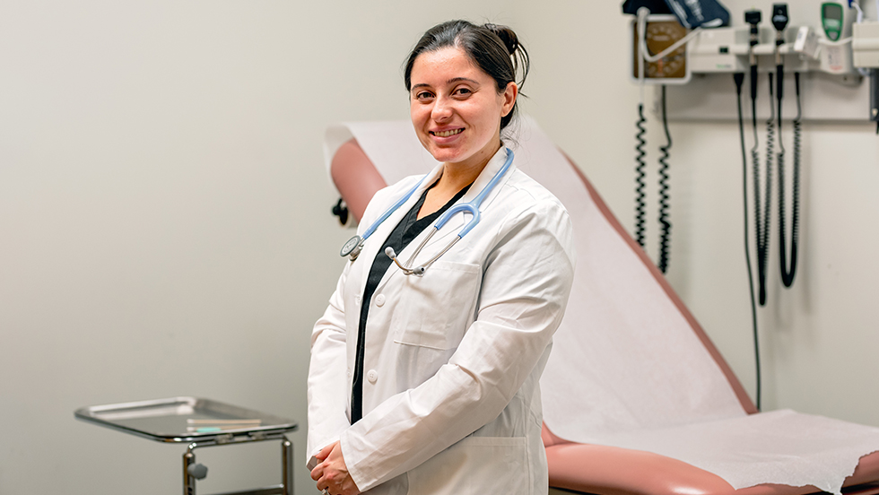Female nursing graduate student wearing a white lab coat and stethoscope in a medical office.