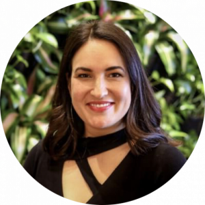 Headshot photo of a woman smiling wearing professional attire in front of a greenery backdrop.