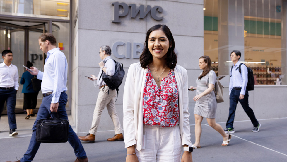 A young woman in business attire poses for the camera on a busy sidewalk in Midtown Manhattan.