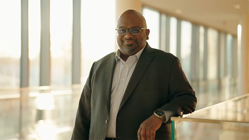 A well-dressed man with a proud smile poses in the hallway of the Nexus building, home of Adelphi's national ranked nursing program.