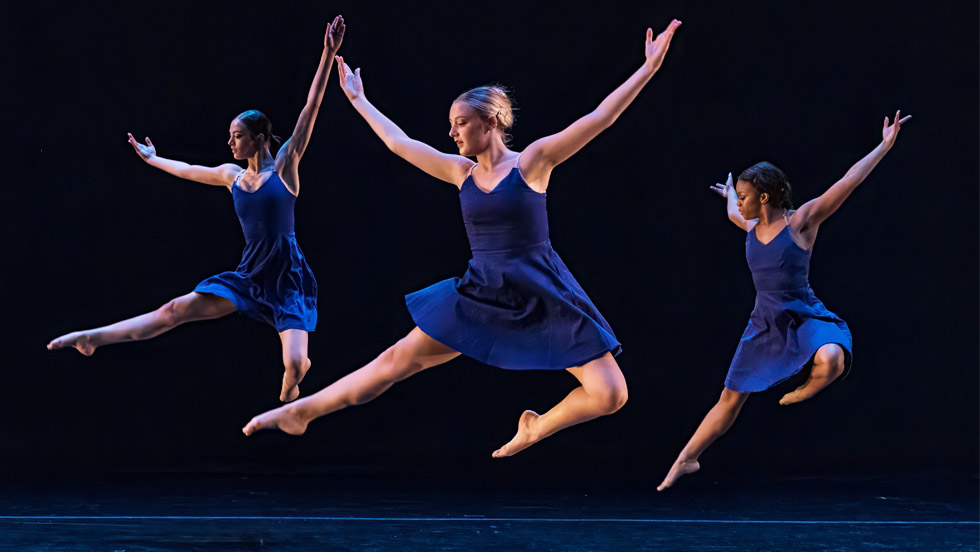 Three women dancers leap in unison, arms overhead.