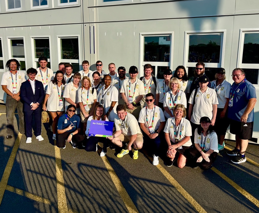 A large group of staff members in matching white uniforms gather after the final World Cup game for a celebratory photo .