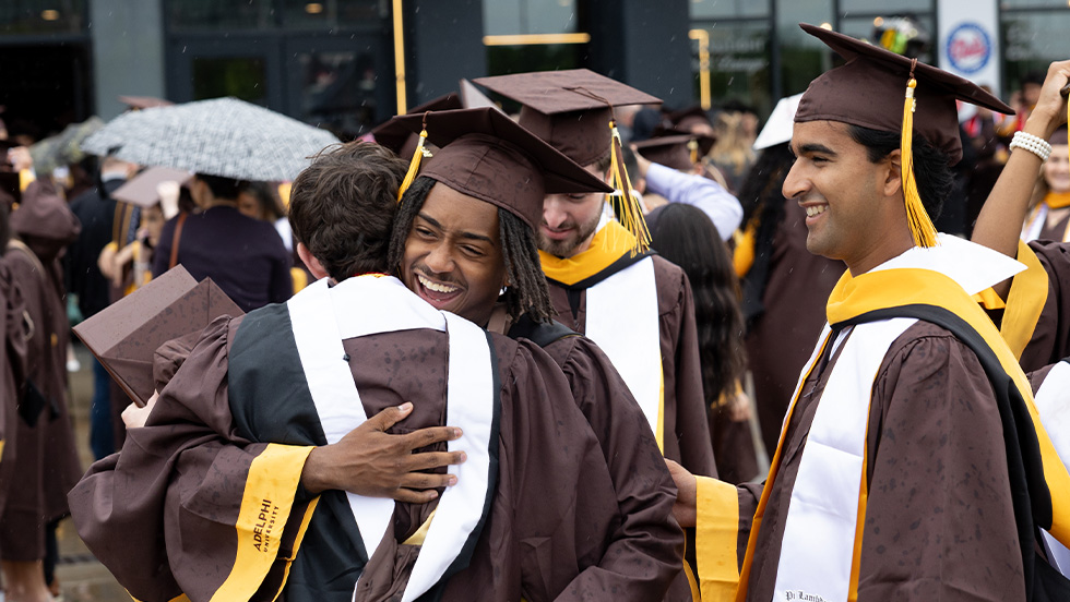 Students wearing graduation attire hugging and celebrating