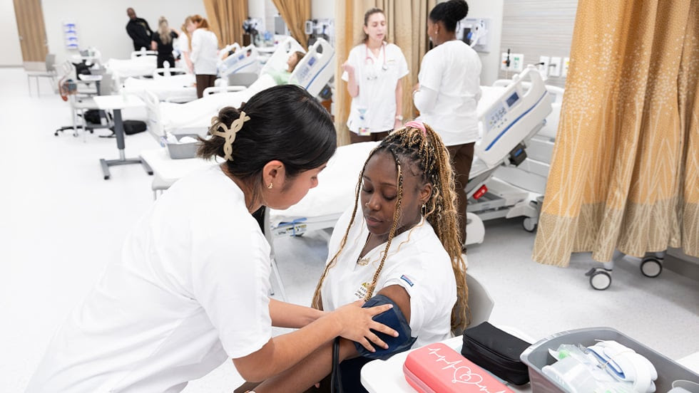 Nursing Leadership: Manhattan Center simulation lab for nursing students. Student taking blood pressure of another nursing student.