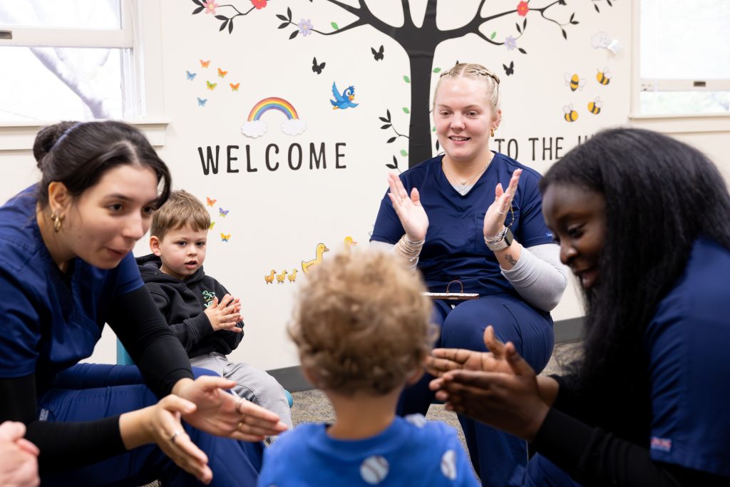 Adelphi SLP students wearing scrubs engaging with children with speech and language delays.