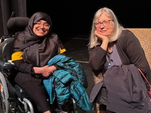 Afra Masud, in her wheelchair and wearing a hijab, next to a seated Alice Hoffman