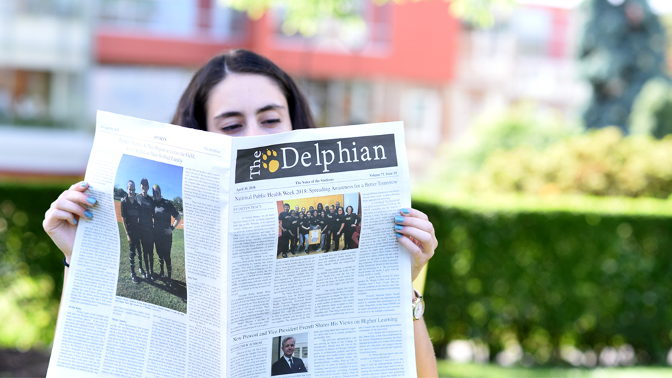 A student reads a copy of the paper on a sunny day on campus.