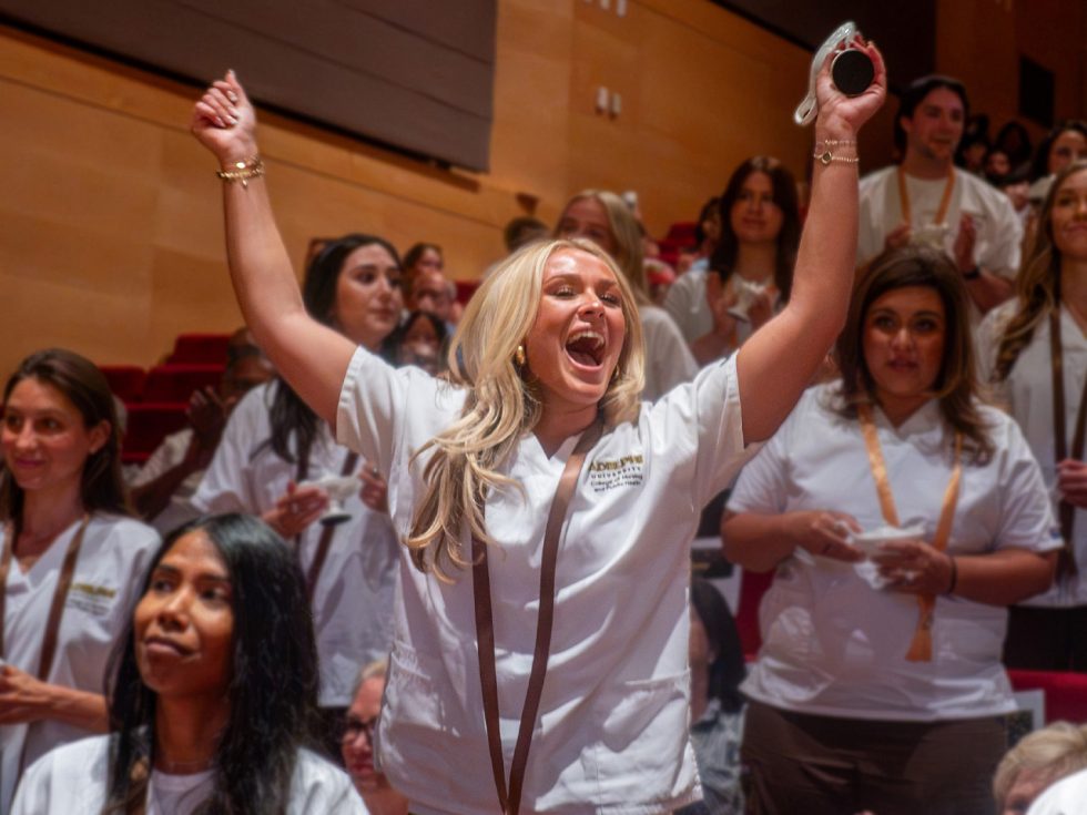 A nursing grad raises her arms and cheers, surrounded by happy classmates.