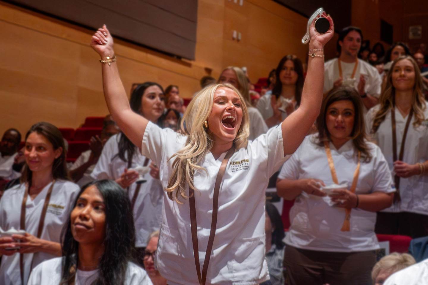 A nursing grad raises her arms and cheers, surrounded by happy classmates.
