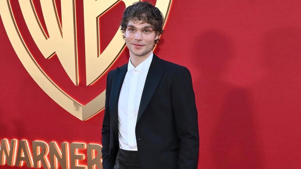 A tall young man in an elegant tuxedo stands on the red carpet