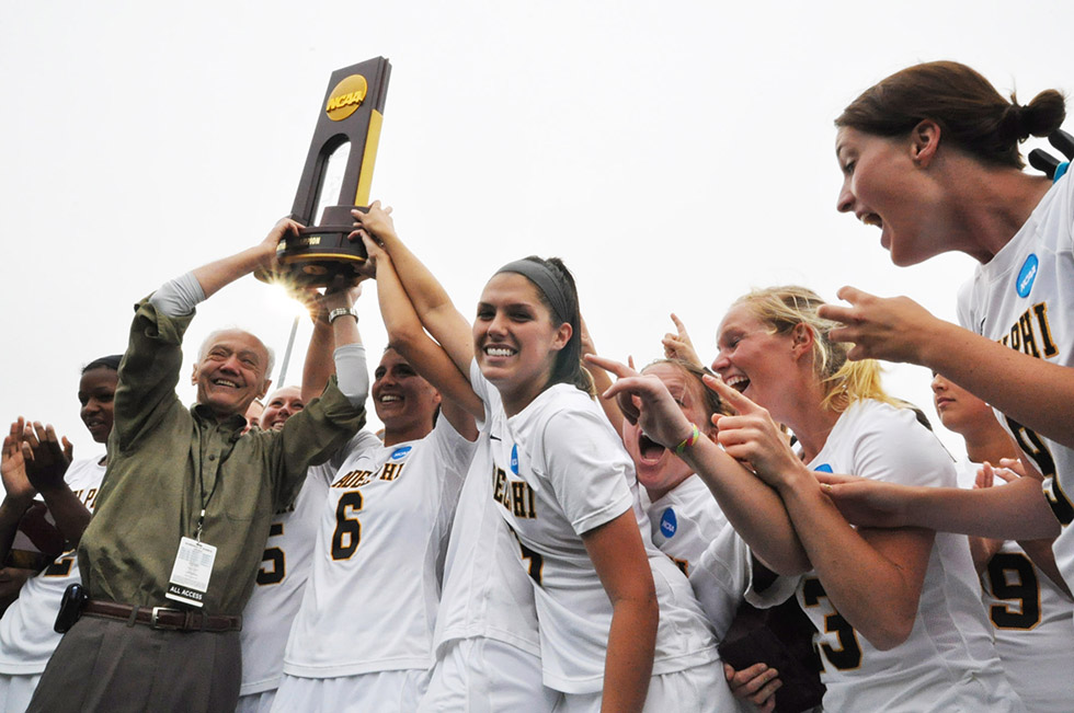 Team members cheer as their coach raises the championship trophy.