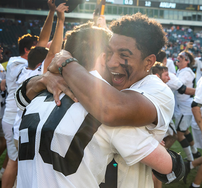 Lacrosse player Kyle Lewis hugs a teammate on-field following Adelphi's win in the 2025 NCAA Championship game.